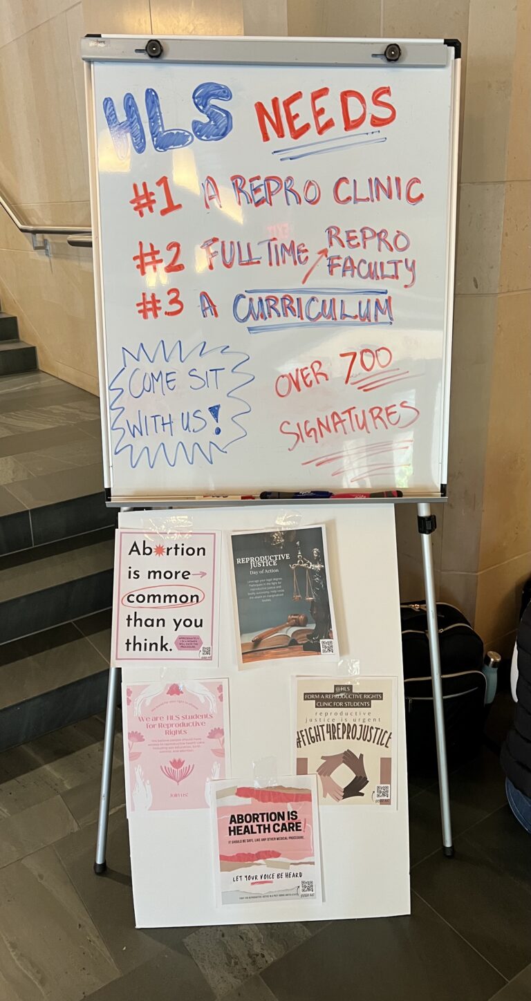 Whiteboard that says that HLS needs a repro clinic, full-time repro faculty, and a repro curriculum. The whiteboard also has messages asking students to come sit and mentioning that the letter has over 700 signatures.