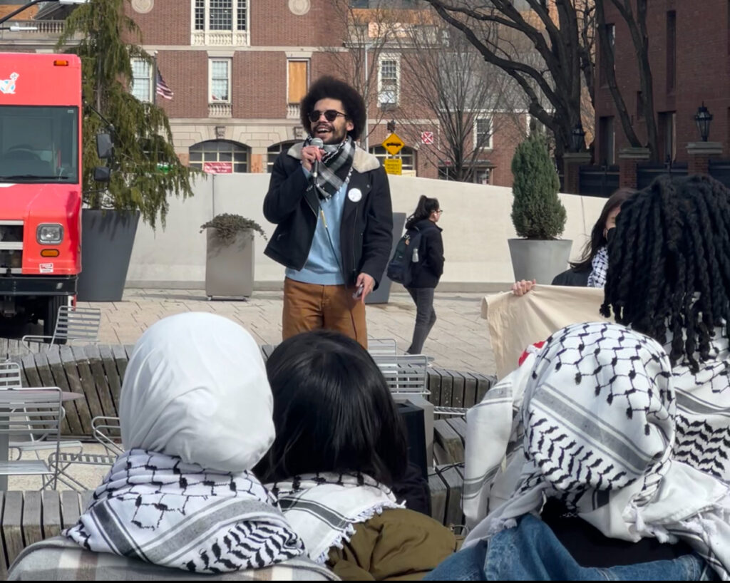 Prince Aviunce Williams, BA '25, (centered, with blue shirt and sunglasses) speaks to a crowd in the Science Center plaza. (Tobi Omotoso, HLS '25)