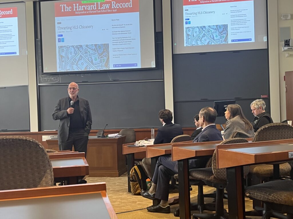 Various attendees of Vigorous Public Interest Day in Langdell Hall, with Deepak Gupta speaking on the screen at the front of the room. (O. Omotoso, 2025)