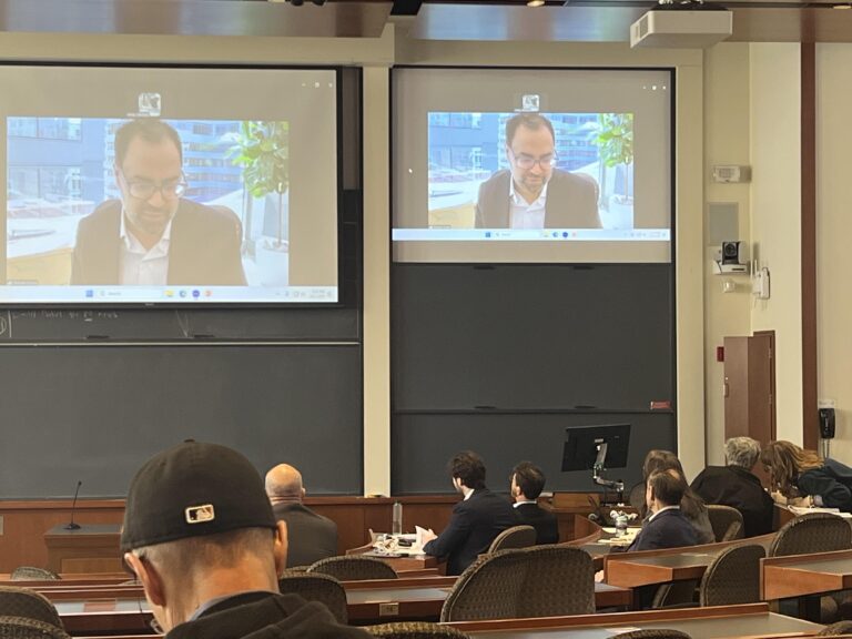 Various attendees of Vigorous Public Interest Day in Langdell Hall, with Deepak Gupta speaking on the screen at the front of the room. (Tobi Omotoso, 2025)