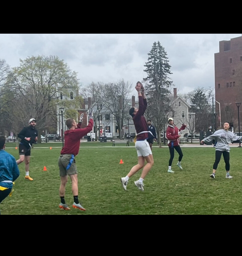 Several flag football players running in Cambridge Common park in the midst of a match.