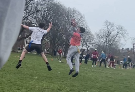 Two players jump for a live ball in the middle of a flag football match in Cambridge Common park. Matt Brandi, HLS '27 (in orange T-shirt and gray underclothes).