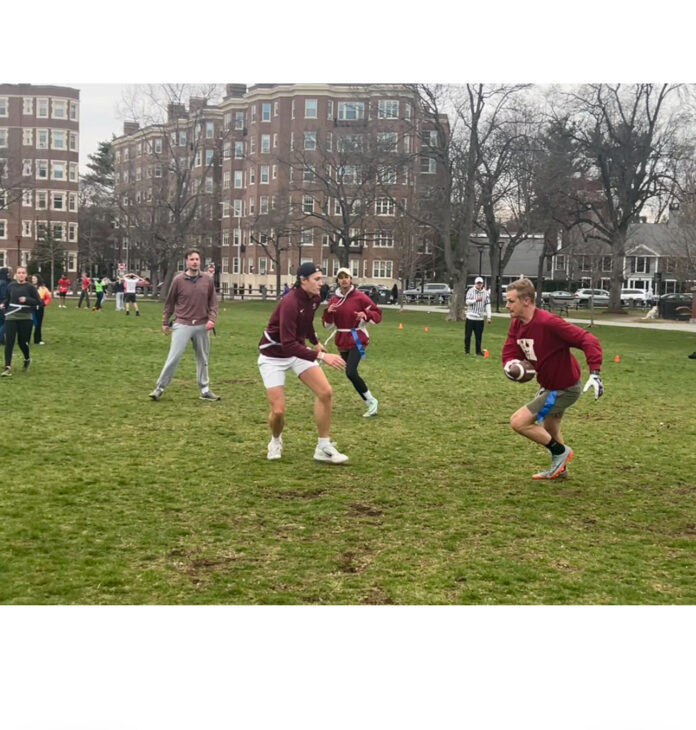 Several flag football players running in Cambridge Common park in the midst of a match. Peter Bell-Goeckner, HLS '25 (, red shirt and gray shorts), and Antoine Beaury, LLM '25 (red shirt, white shorts) prepare to engage each other in play.